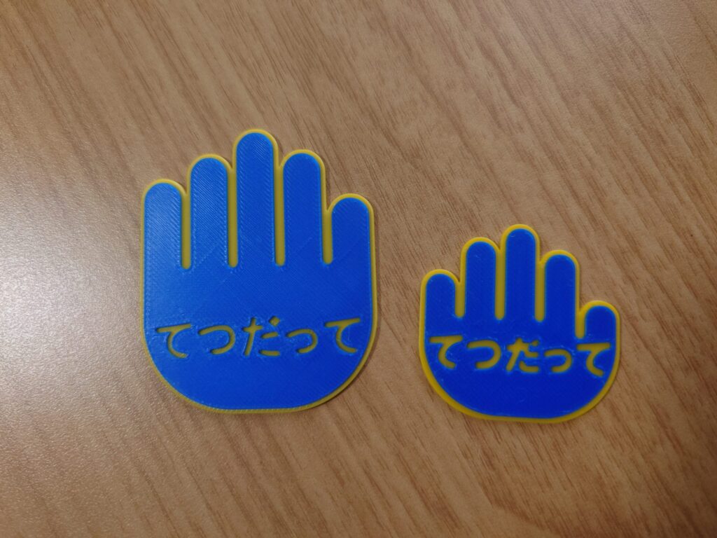 青い手のひらの形をした大小2枚のてつだってカード。黄色の文字と縁取り