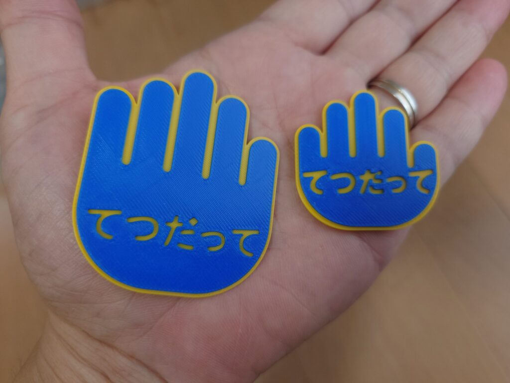 手のひらに載せた大小のてつだってカード。大は縦60×横50mm、小は縦40×横40mm