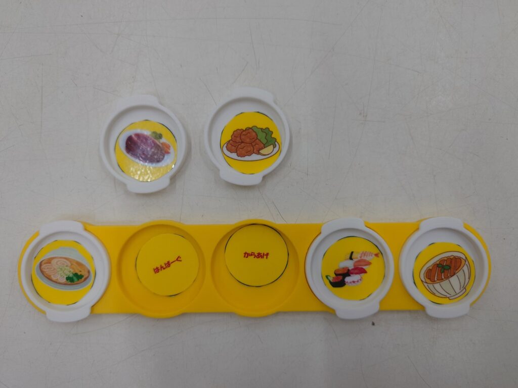ことばを入れた黄色いプレートに、料理の絵を入れた白い小皿を3つはめた写真